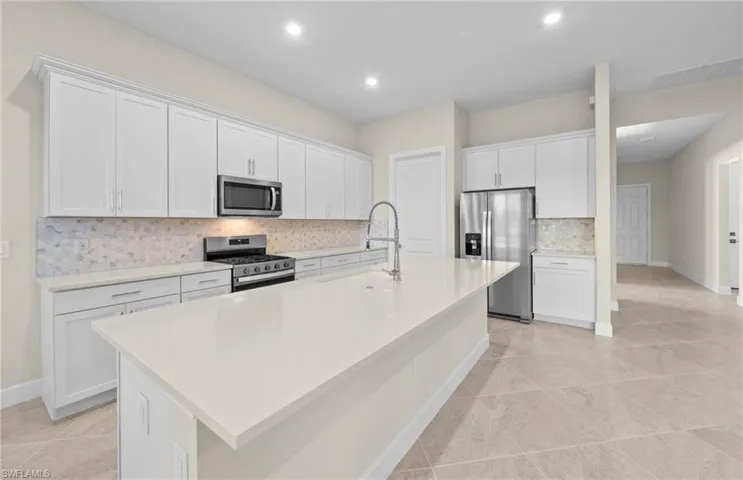 Kitchen featuring decorative backsplash, white cabinetry, stainless steel appliances, a center island with sink, and light stone counters