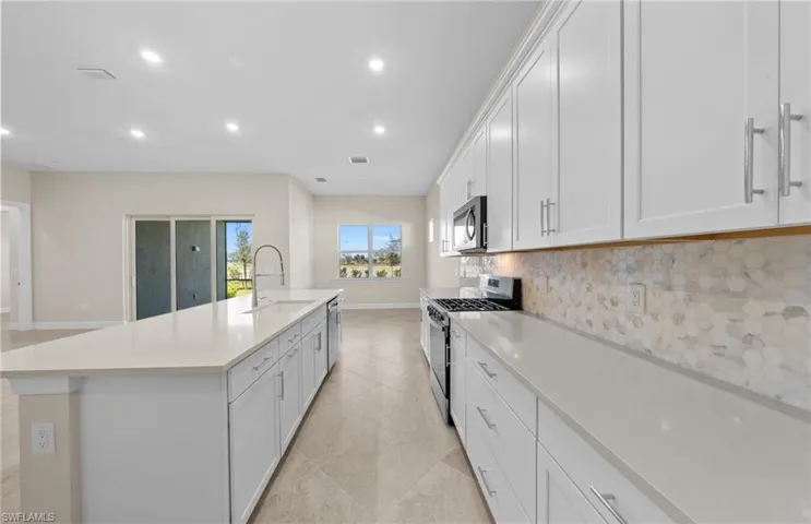 Kitchen featuring stainless steel appliances, a large island with sink, recessed lighting, light stone countertops, and backsplash