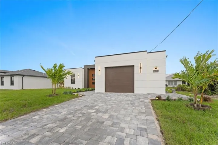 Contemporary home featuring a garage, decorative driveway, a front lawn, and stucco siding