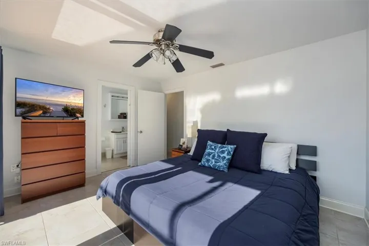 Tiled bedroom featuring ceiling fan, ensuite bath, visible vents, and baseboards