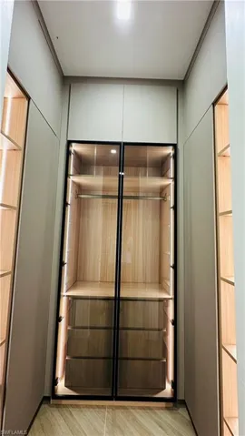Built-in wardrobe with glass-front doors, integrated lighting, wood-finish shelving, and pull-out drawers