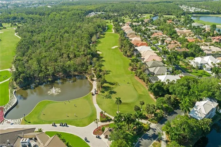 Aerial perspective featuring an expansive golf course, water feature with a fountain, manicured landscaping, and mature foliage