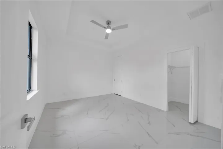Unfurnished bedroom featuring a walk in closet, a ceiling fan, marble finish floors, and a tray ceiling