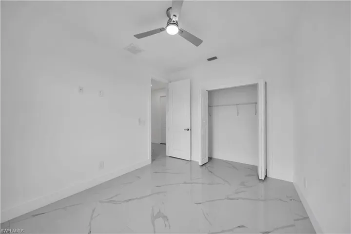 Unfurnished bedroom featuring ceiling fan, light marble finish floors, and a closet