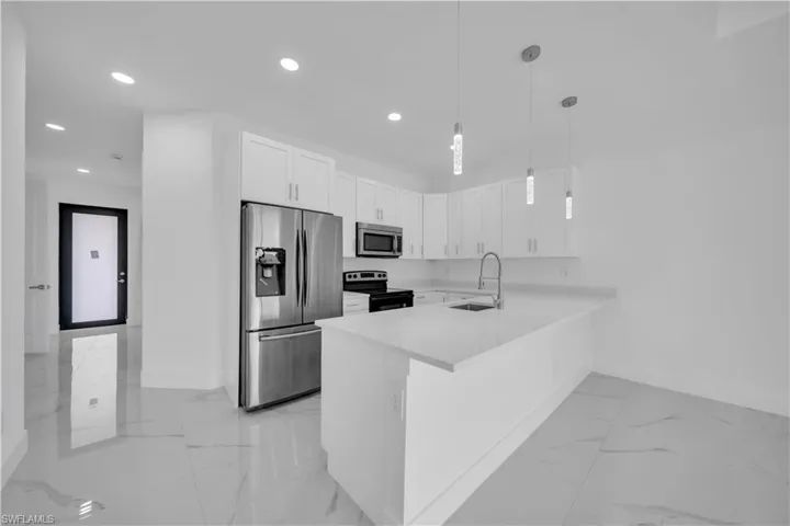 Kitchen featuring stainless steel appliances, white cabinetry, decorative light fixtures, light stone counters, and a peninsula