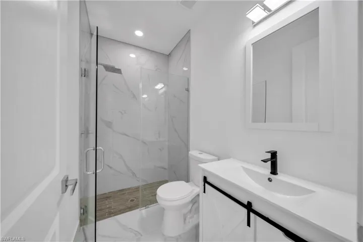 Full bath featuring vanity, a marble finish shower, marble look tiles, and recessed lighting