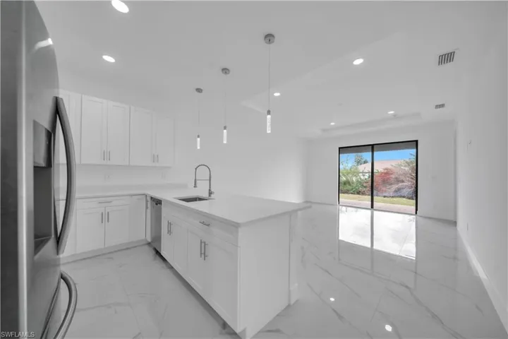 Kitchen featuring stainless steel appliances, decorative light fixtures, white cabinetry, light stone countertops, and a tray ceiling