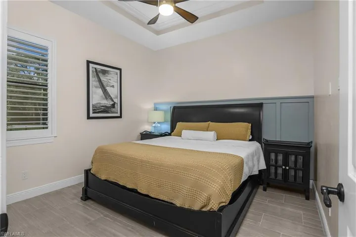 Guest bedroom #1 featuring plantation shutter, tray ceiling with crown molding, & custom millwork feature wall.