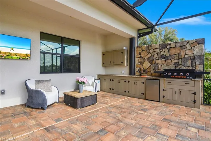 The outdoor kitchen features a blackstone grill, stainless steel refrigerator, sink, and plenty of storage space.
