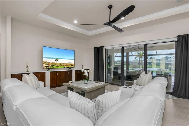 Large great room features a custom built in providing additional storage, tray ceiling with crown molding, and pocketing impact sliders for seamless indoor/outdoor living.