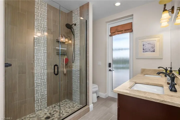 Guest bath also serves as the pool bath with an outdoor entry for convenience and features custom tile-work and a frameless walk-in shower.