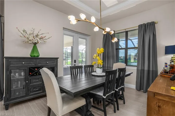 Enjoy dining in this inviting space which includes tray ceiling with crown molding, designer lighting, and double entry doors leading to the outdoor lanai space.