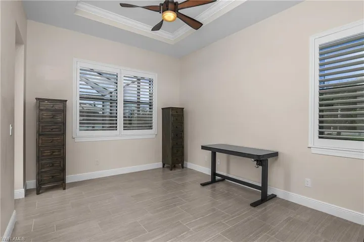 Guest bedroom #2 with tray ceiling/crown molding, plantation shutters, and door to outdoor living space.
