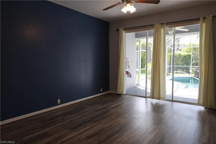 Spacious interior room with dark wood-finish flooring, a deep blue accent wall, and a ceiling fan with integrated lighting