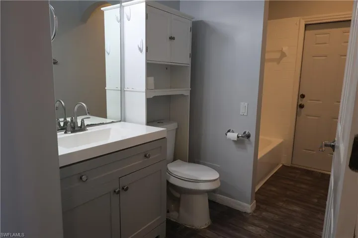 Bathroom featuring a white integrated sink, gray vanity with cabinet storage, chrome faucet, wood-finish flooring, and a white tiled shower surround