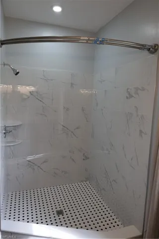 Shower stall featuring white subway tile with subtle grey veining, black and white mosaic floor tile, and a built-in corner shelf