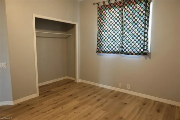 Room featuring wood-finish flooring, a window, and a built-in closet with shelving and hanging rod