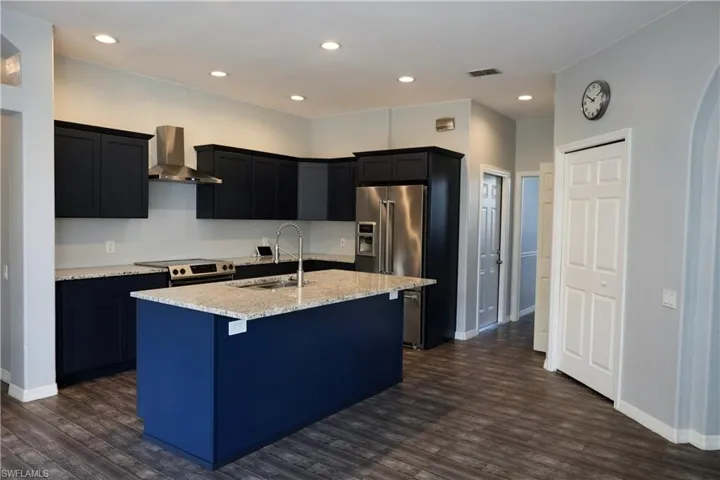 Kitchen featuring a center island with a sink, light-toned countertops, dark cabinetry, stainless steel appliances, and wood-finish flooring