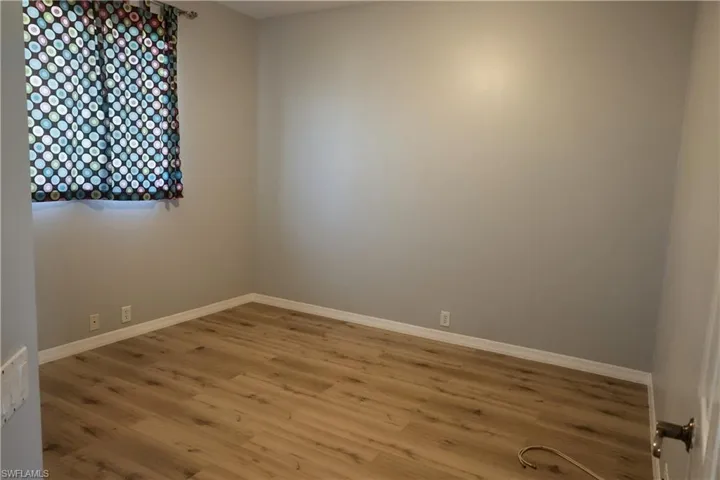 Room with wood-finish flooring, light grey walls, and white baseboards