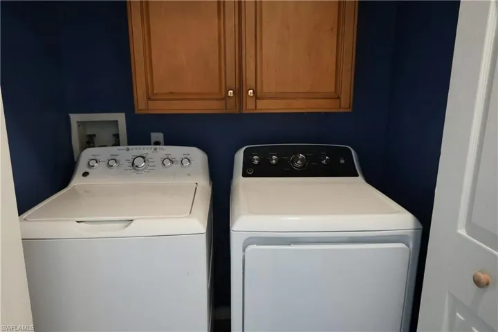 Dedicated laundry area featuring overhead wood cabinetry and a rich blue wall finish