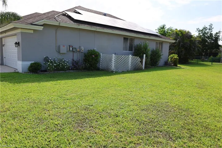 Spacious grassy yard with solar panels on the roof, a two-car garage, and established landscaping