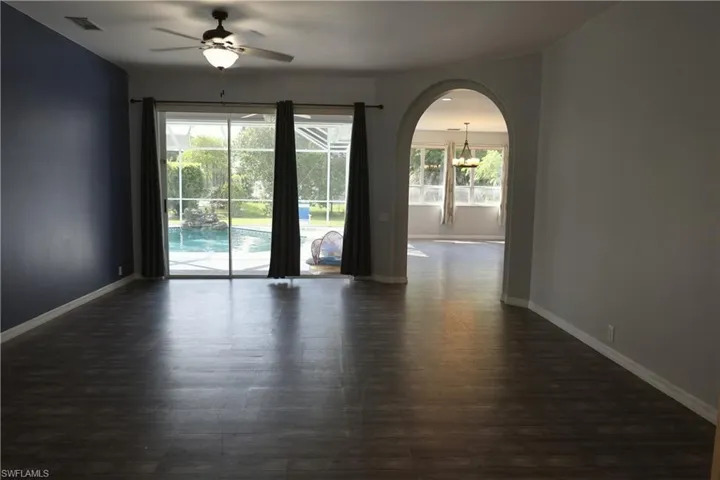Spacious interior featuring wood-finish flooring, a contemporary ceiling fan, and sliding glass doors revealing a screened pool enclosure