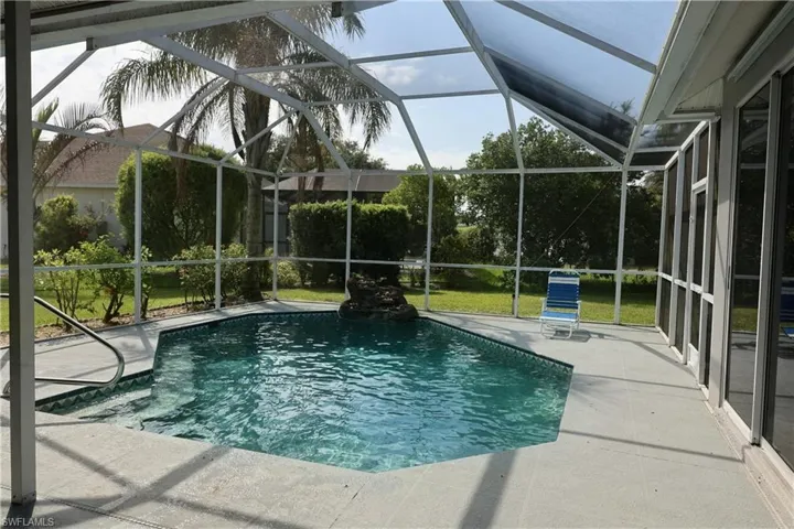Screen-enclosed pool area featuring a freeform swimming pool with a rock waterfall feature and integrated steps with a handrail