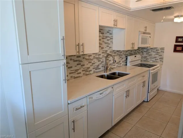 Kitchen featuring white appliances, white cabinets, decorative backsplash, and light tile patterned floors