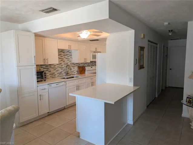 Kitchen featuring decorative backsplash, light tile patterned floors, white appliances, white cabinets, and a peninsula