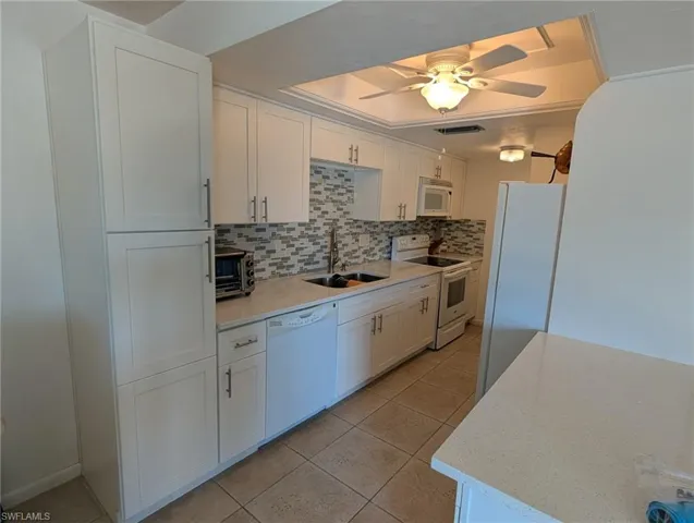Kitchen with white cabinetry, white appliances, tasteful backsplash, and light stone countertops