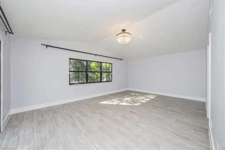 Empty room with lofted ceiling, light wood-style floors, and a chandelier