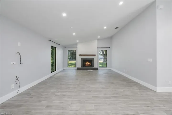 Unfurnished living room with lofted ceiling, recessed lighting, a warm lit fireplace, and wood tiled floors