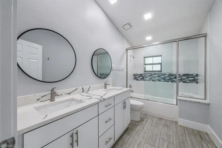 Bathroom featuring bath / shower combo with glass door, double vanity, and wood finish floors