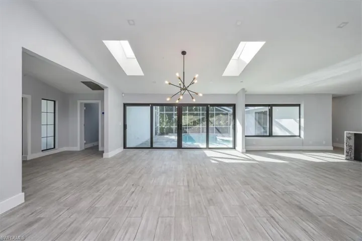 Unfurnished living room with a chandelier, wood finish floors, lofted ceiling, and a skylight