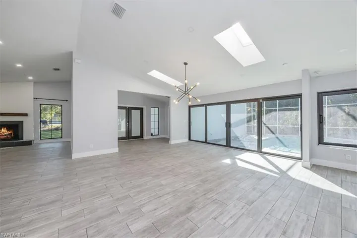 Unfurnished living room with a chandelier, a lit fireplace, a skylight, wood finish floors, and high vaulted ceiling