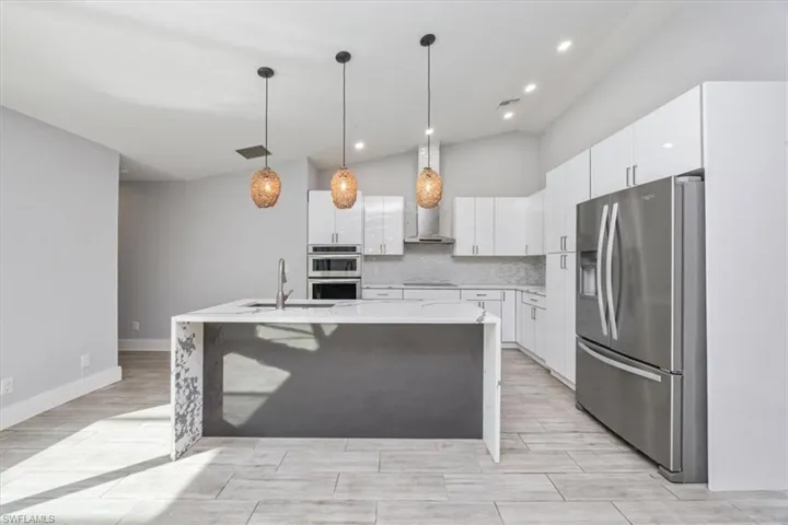 Kitchen featuring stainless steel appliances, decorative light fixtures, light stone counters, vaulted ceiling, and white cabinets