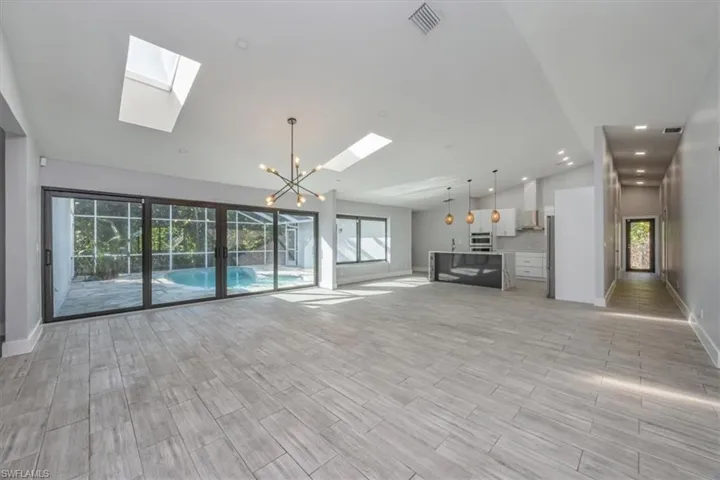 Unfurnished living room with a chandelier, healthy amount of natural light, lofted ceiling, wood tiled floors, and a skylight