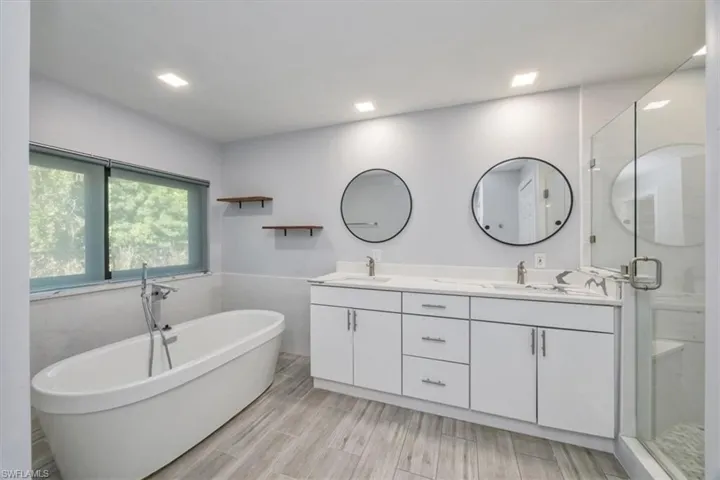 Full bath featuring double vanity, a freestanding tub, wainscoting, a stall shower, and wood tiled floors