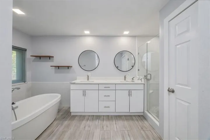 Bathroom with a stall shower, a freestanding bath, double vanity, wainscoting, and wood finish floors