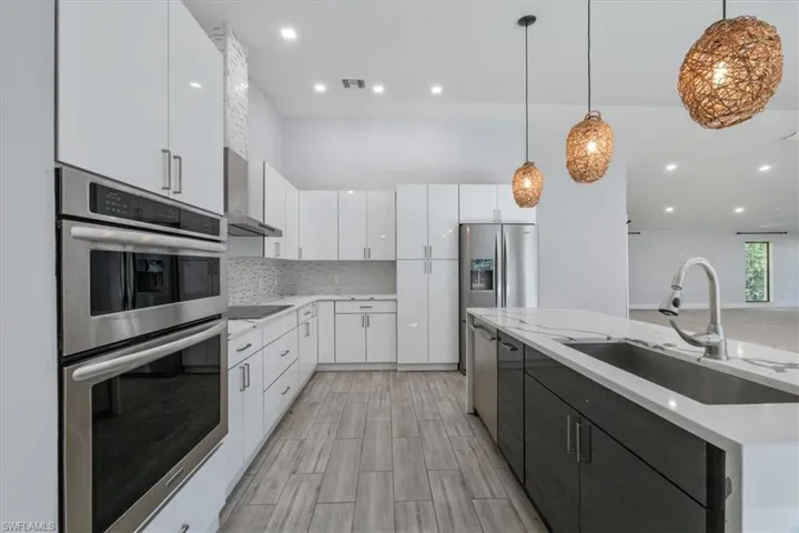 Kitchen with stainless steel appliances, white cabinetry, hanging light fixtures, a kitchen island with sink, and recessed lighting