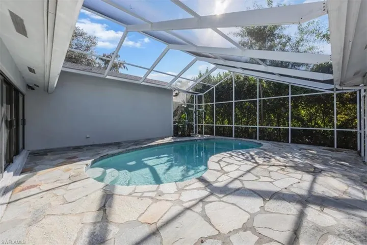 Outdoor pool featuring a sunroom, a patio area, and glass enclosure