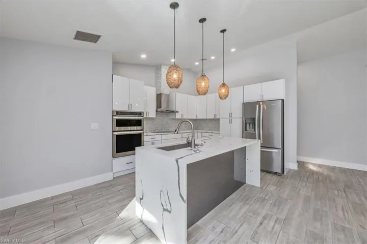 Kitchen with appliances with stainless steel finishes, decorative light fixtures, white cabinets, an island with sink, and light stone countertops