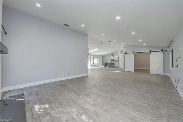 Unfurnished living room featuring a barn door, recessed lighting, wood tiled floors, and lofted ceiling