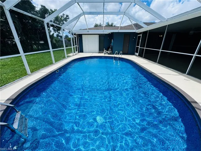 View of pool with a lawn and glass enclosure