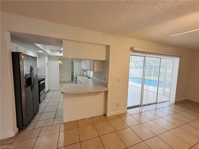 Kitchen with appliances with stainless steel finishes, kitchen peninsula, a textured ceiling, light tile patterned flooring, and ceiling fan