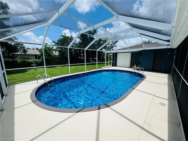 View of pool featuring glass enclosure, a lawn, and a patio area