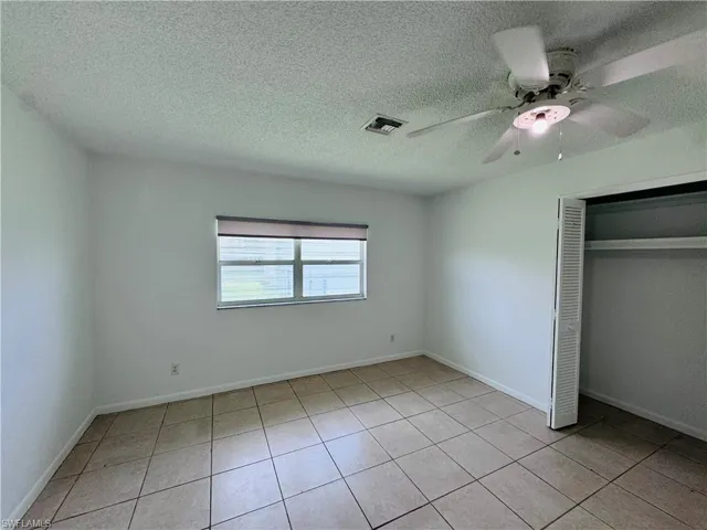 Unfurnished bedroom with a closet, a textured ceiling, ceiling fan, and light tile patterned floors