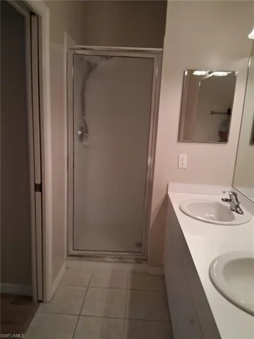Bathroom with double vanity, a shower stall, and light tile patterned floors