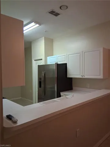 Kitchen with light countertops, stainless steel fridge with ice dispenser, and white cabinetry