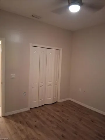 Unfurnished bedroom with dark wood-type flooring, a closet, and a ceiling fan